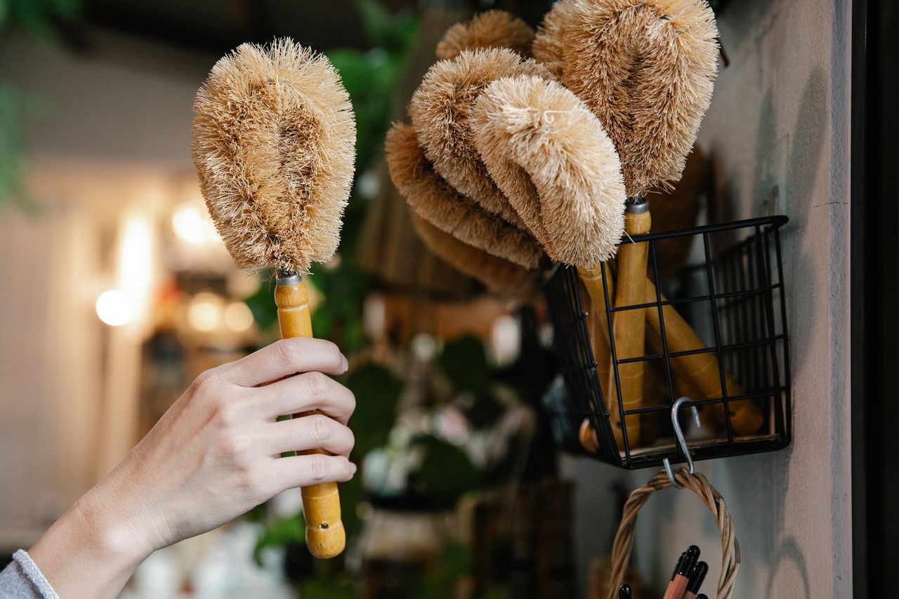 services-04 Close-up of a hand selecting eco-friendly cleaning brushes from a basket indoors.
